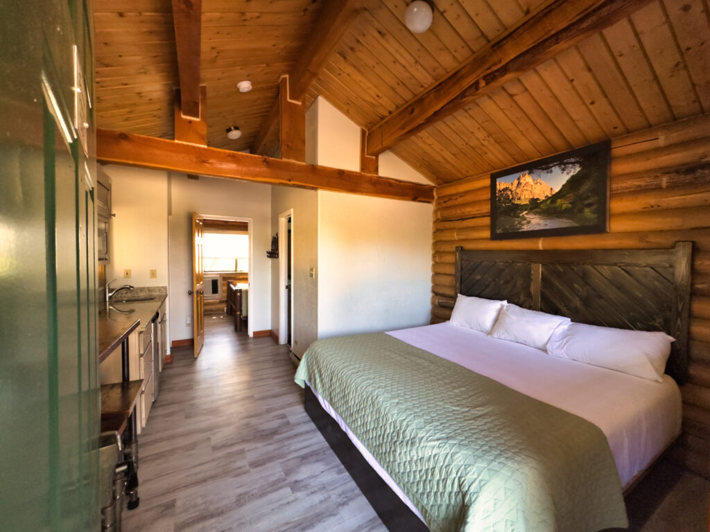 A cozy wooden cabin interior featuring a queen-sized bed and a kitchenette.